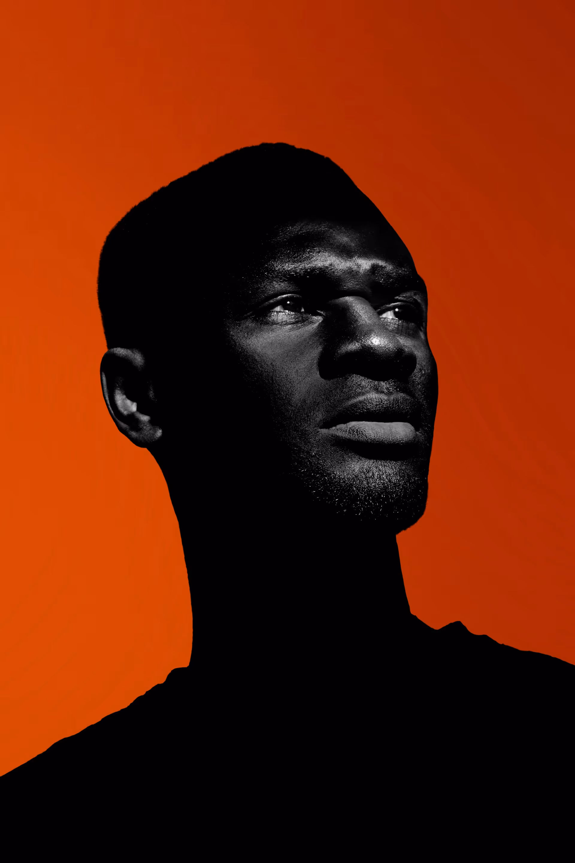 Close-up silhouette of a man looking thoughtfully to the side against an orange background.