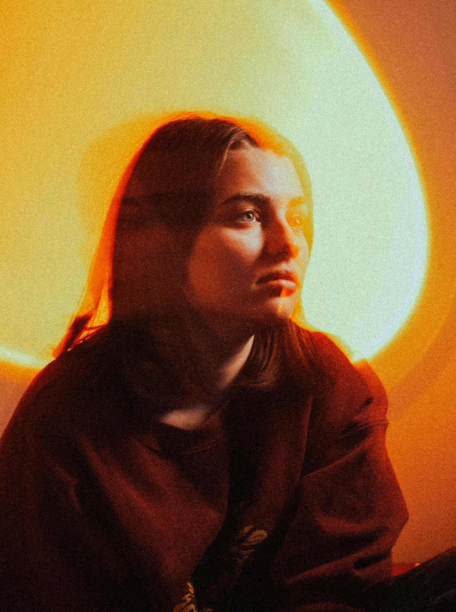 Portrait of a woman with shoulder-length hair gazing to the side, with warm, artistic lighting creating a glowing halo effect behind her.